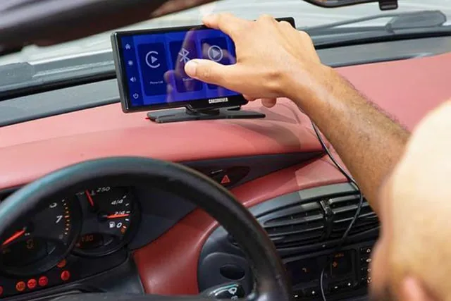 Hand holding smartphone next to car infotainment screen for comparison